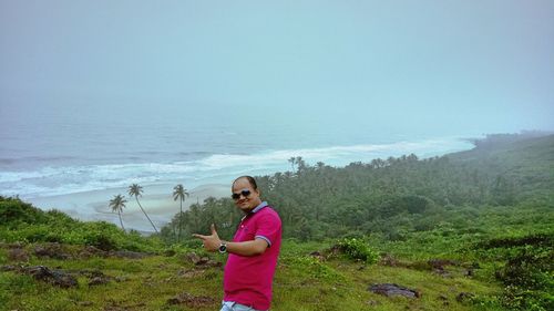 Man gesturing while standing on mountain against sea during foggy weather