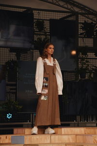 Young woman looking down while standing against built structure