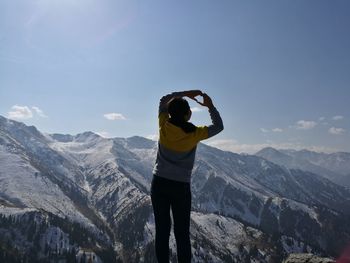 Rear view of woman making heart shape while standing on mountain