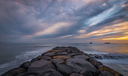 Rocks on sea shore against sky during sunset