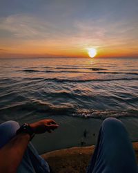 Midsection of man sitting at beach during sunset