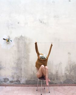 Woman sitting on chair against wall