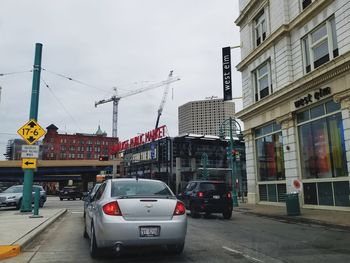 Cars on city street by buildings against sky