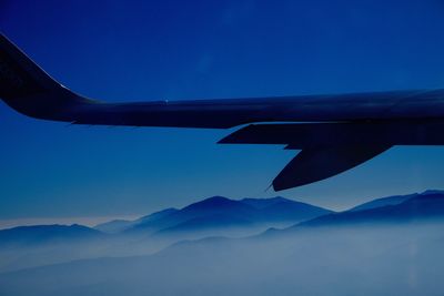 Cropped image of aircraft wing over mountains against sky at dawn