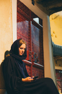 Young woman wearing traditional clothing while using phone against closed door