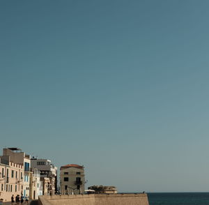 Buildings by sea against clear blue sky