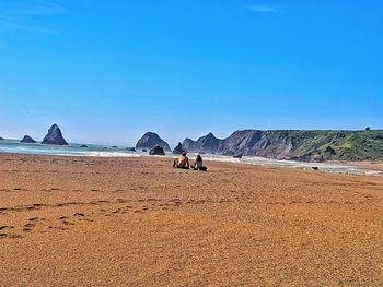 Rear view of people sitting at beach against blue sky