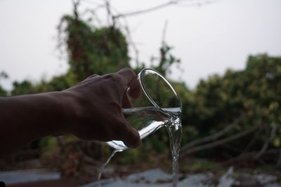 Close-up of hand holding drinking water against trees