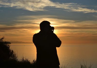 Silhouette woman standing at beach against sky during sunset