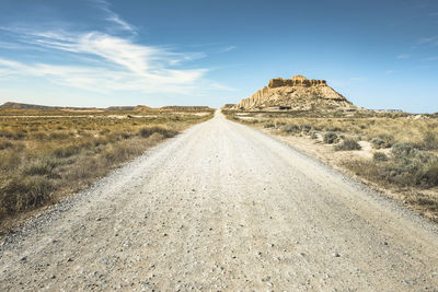 Dirt road leading towards mountain against sky