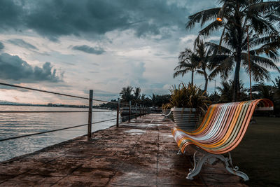 Empty chairs and palm trees by sea against sky