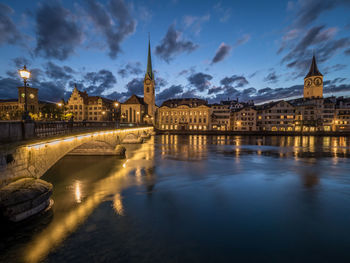 Arch bridge over river in city at dusk