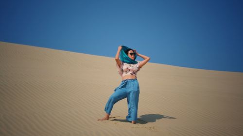 Woman standing on sand dune against clear sky