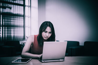 Young woman using mobile phone while sitting on table