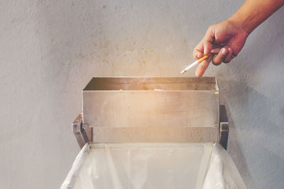 Cropped image of hand throwing cigarette in container