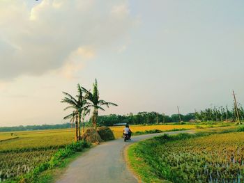 People riding bicycle on road amidst field against sky
