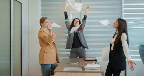 Excited  team people toss papers up stand at office table celebrate corporate success freedom. 