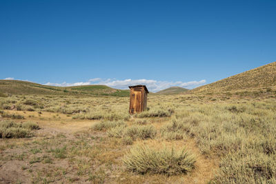 Vintage toilet out house on field against clear blue sky in ghost town