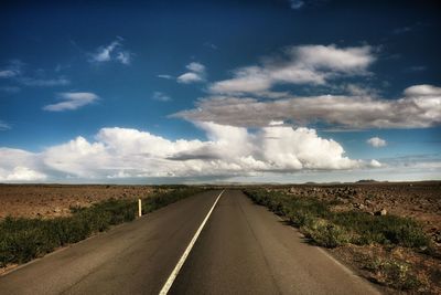 View of country road amidst barren landscape against cloudy sky