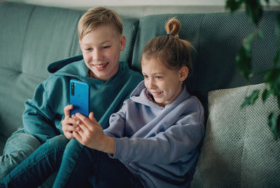 Kids using mobile phone while sitting on sofa at home