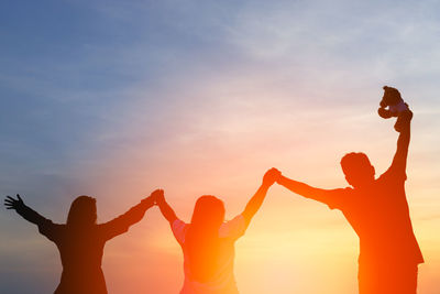 Silhouette people with arms raised against sky during sunset