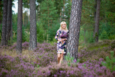 Woman standing by tree amidst purple flowering plants in forest