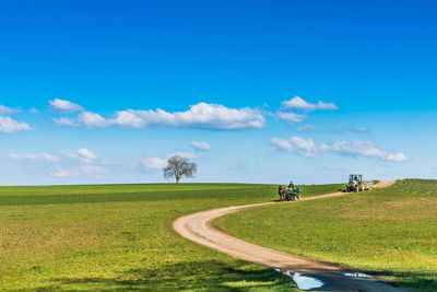 Road passing through field against cloudy sky