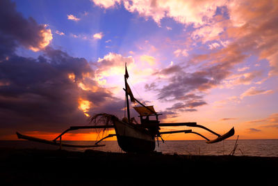 Silhouette boat moored on beach against sky during sunset