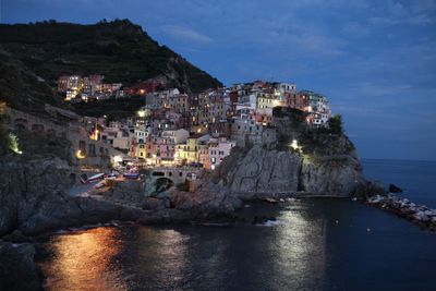 Illuminated cinque terre by sea against sky at dusk