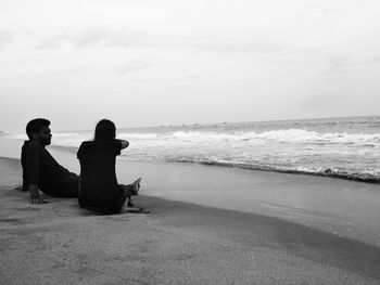 People sitting on beach looking at sea against sky