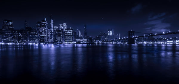 Illuminated bridge over river by buildings against sky at night