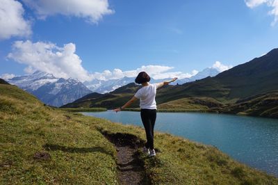 Rear view of woman walking by lake and mountain against sky