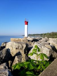 Lighthouse on rock by sea against clear sky