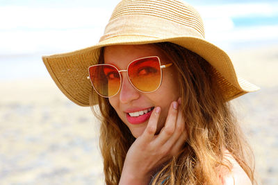 Portrait of smiling young woman wearing sunglasses and hat at beach