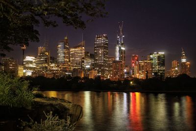 Illuminated buildings by river against sky at night