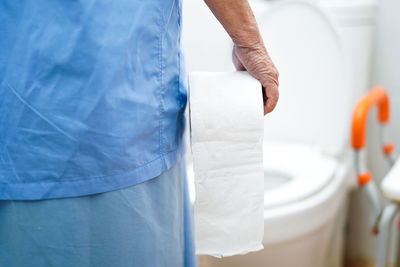 Midsection of female patient holding toilet paper while standing in bathroom