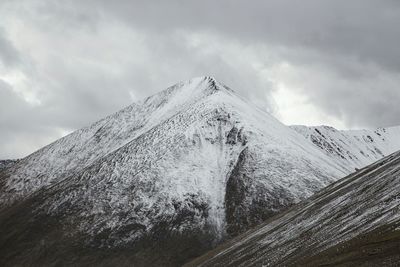 Low angle view of snow covered hill against cloudy sky