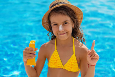 Portrait of smiling girl applying suntan lotion in swimming pool