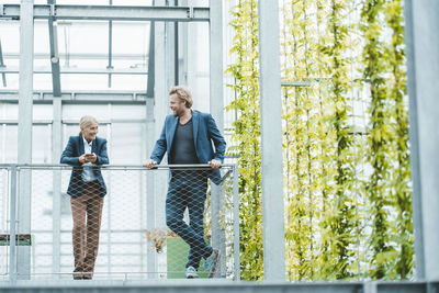 Agronomist discussing with coworker by railing in plant nursery