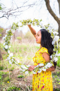 Mixed race african american woman in a yellow dress holding a homemade floral wrapped hula hoop