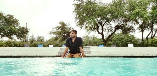 Woman standing by swimming pool against trees