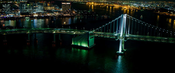 Illuminated bridge over river in city at night