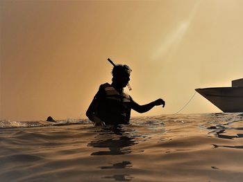 Silhouette man in sea against sky during sunset