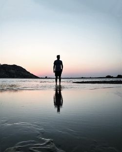 Rear view of silhouette man standing at beach against sky