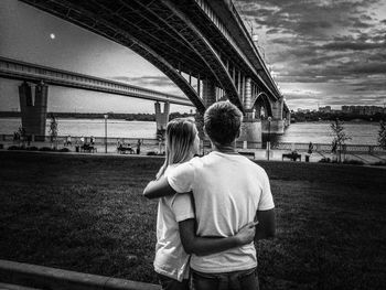 Rear view of man and woman looking at bridge against sky