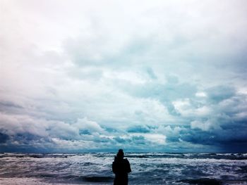 Man standing on beach against cloudy sky