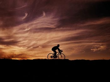 Silhouette man riding bicycle against sky during sunset