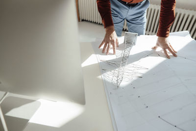 Hands of engineer by electricity pylon model on blueprint at desk