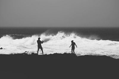Silhouette people at beach against clear sky