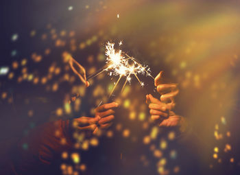 Cropped hands of people holding sparkler at night